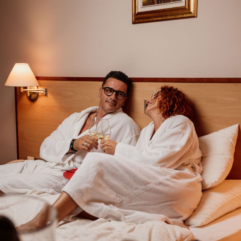 Par u kupaćim ogrtačima nazdravlja u hotelskom krevetu